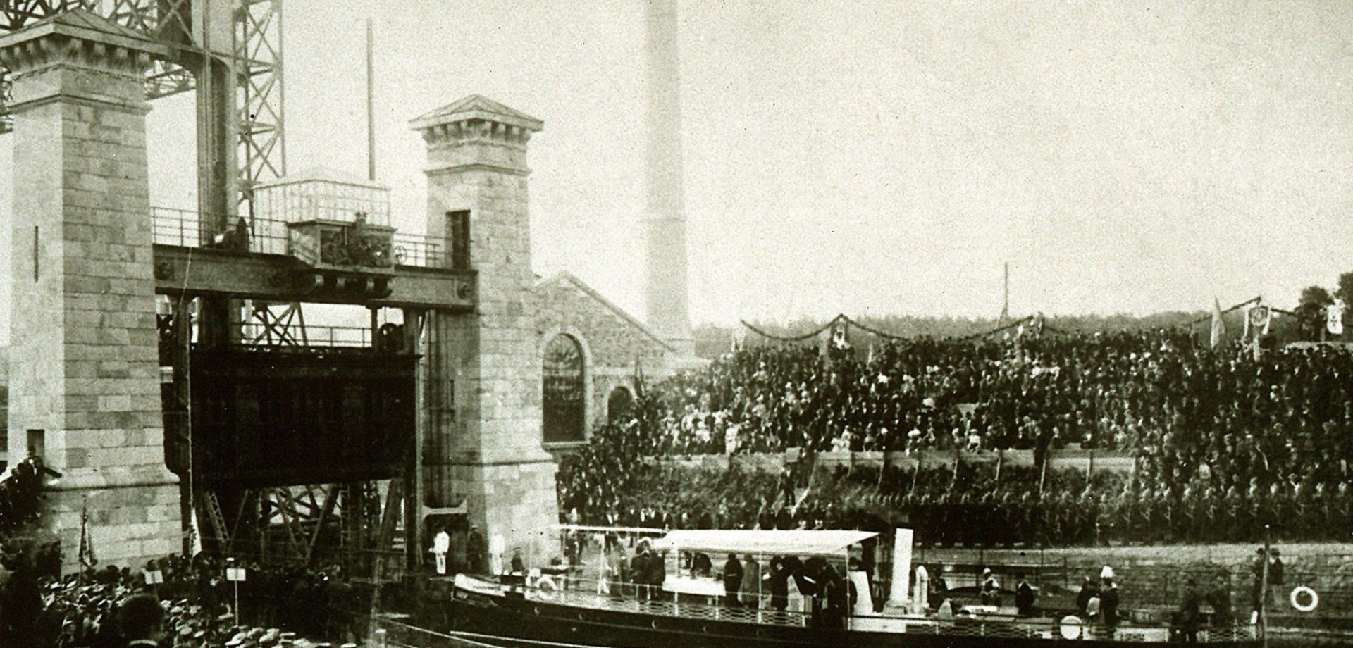 Schwarz-Weiß Aufnahme der Eröffnung des Schiffshebewerkes im Jahre 1899 mit hunderten Menschen am Ufer des Kanals.