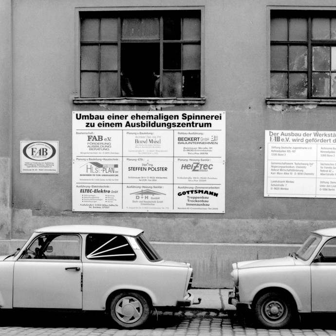 Schwarz-Weiß Fotografie von zwei parkenden Trabbis vor einer ehemaligen Spinnerei. (öffnet vergrößerte Bildansicht)