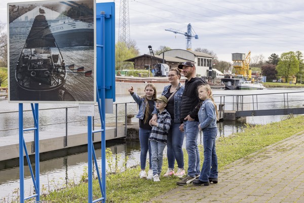 Familie steht am Kanal vor einer Steele.