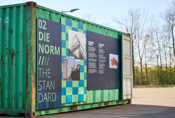 Container auf dem Außengelände mit einer Texttafel auf der "DIE NORM" steht.