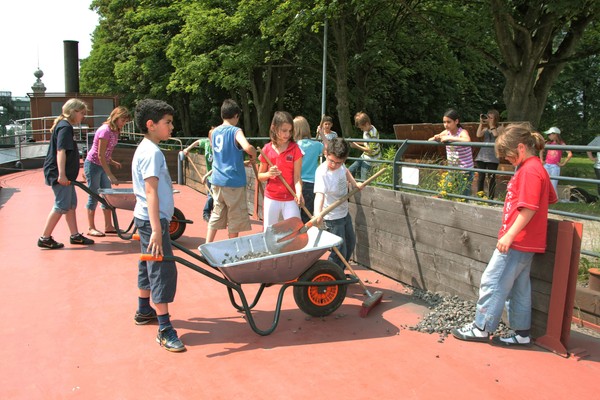 Kinder arbeiten mit einer Schubkarre an Deck des Museumsschiffes.