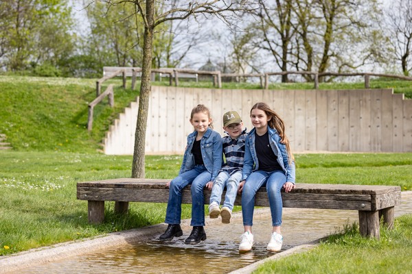 Drei Kinder sitzen auf einer Brücke über einem kleinen Wasserlauf.